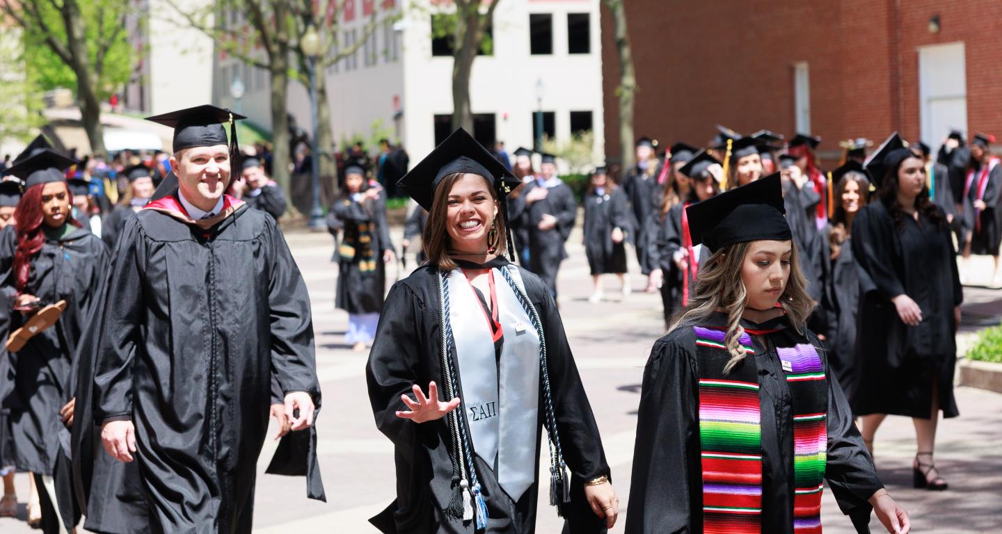 graduate students walking with diplomas at commencement