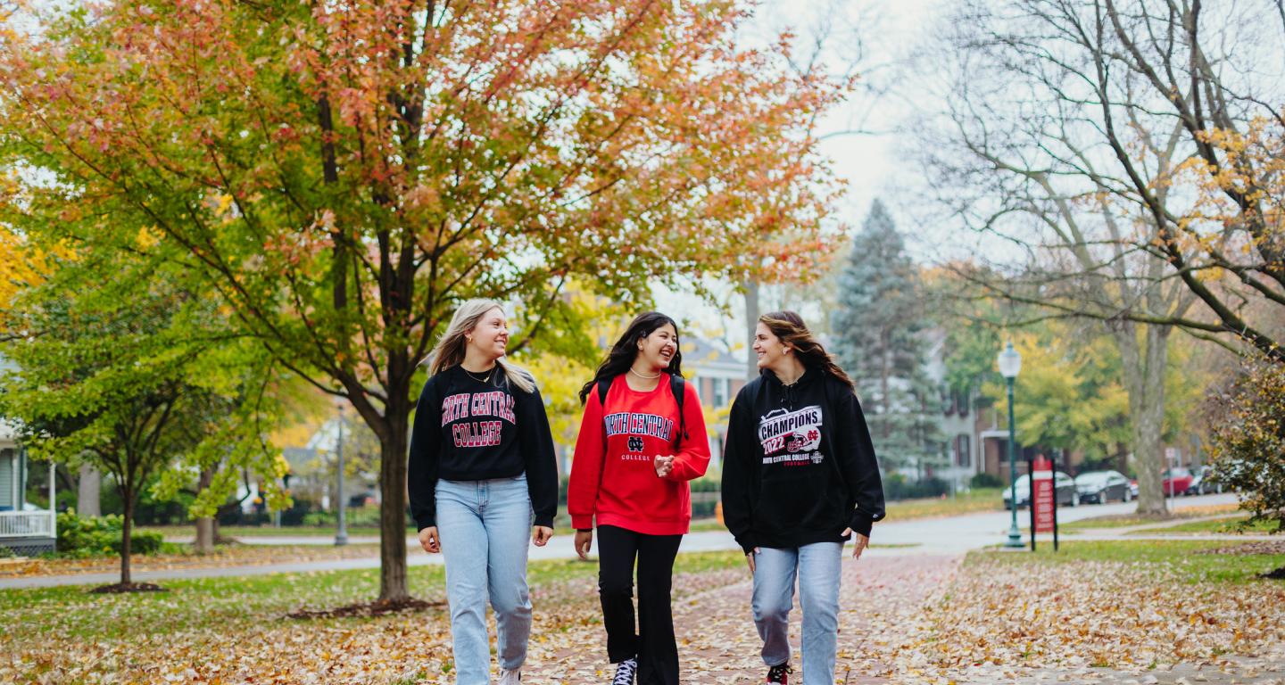 Three North Central College students are walking down a path on campus.